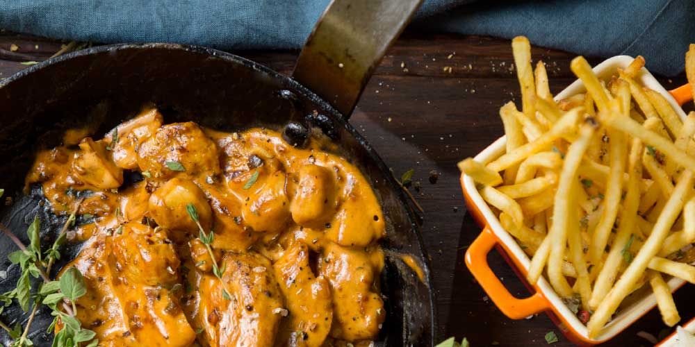 A skillet of meat covered in a cream sauce and a side of fries, looks delicious. 