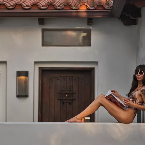 Woman sitting on ledge sipping a cocktail outside hotel room door at the Sunset Marquis